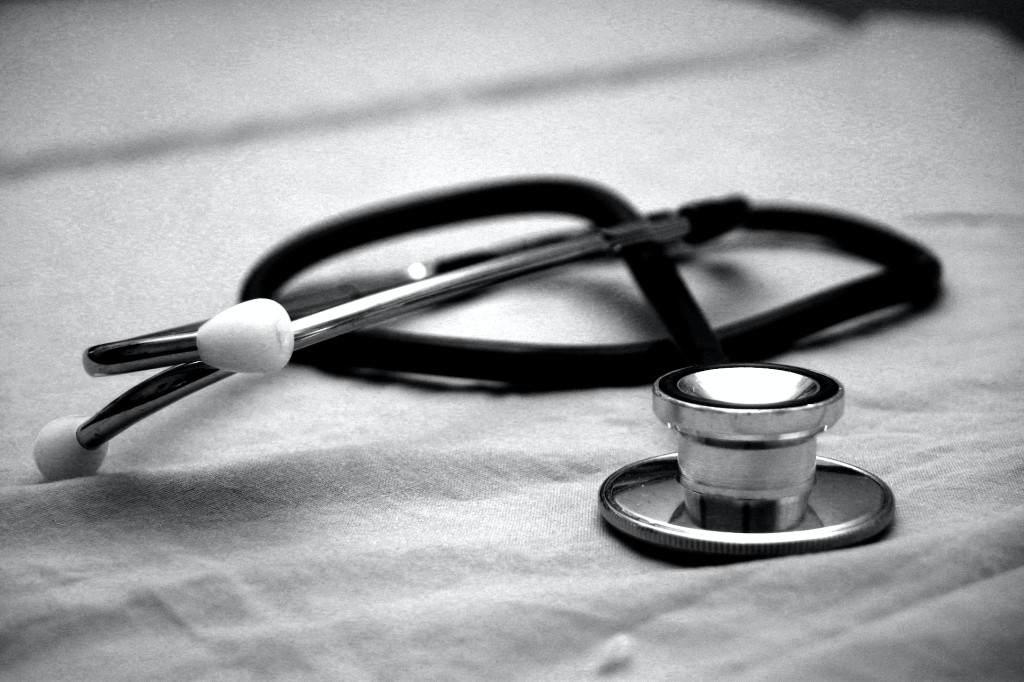 Black and white close-up of a medical stethoscope resting on a clinical fabric surface